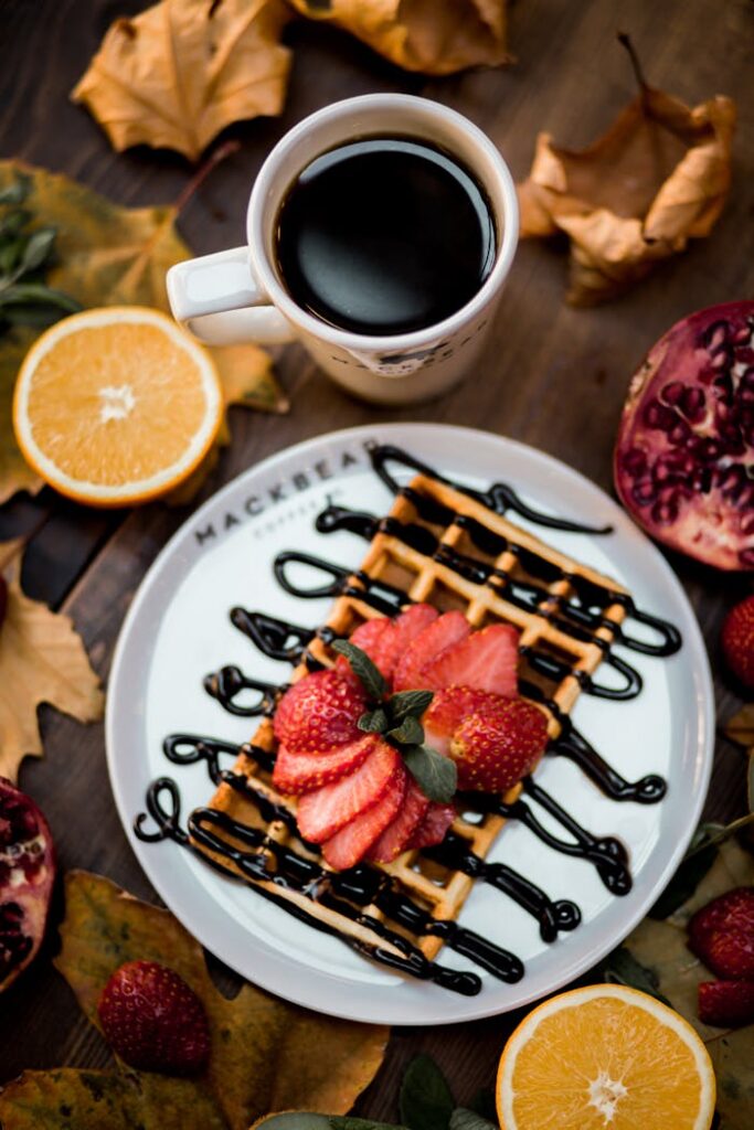 pexels-photo-14705142 Waffle topped with strawberries and chocolate sauce, surrounded by fruits and coffee for a cozy breakfast setting.