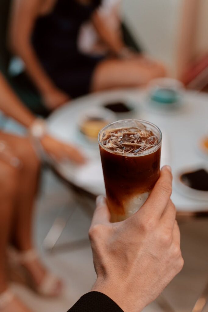 pexels-photo-4921528 A hand holds an iced coffee during an indoor cafe gathering, featuring a blend of lively conversation and modern style.