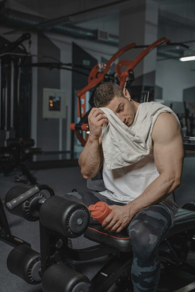 pexels-photo-5327546-5327546 A muscular man in a gym resting and wiping sweat with a towel after a workout.