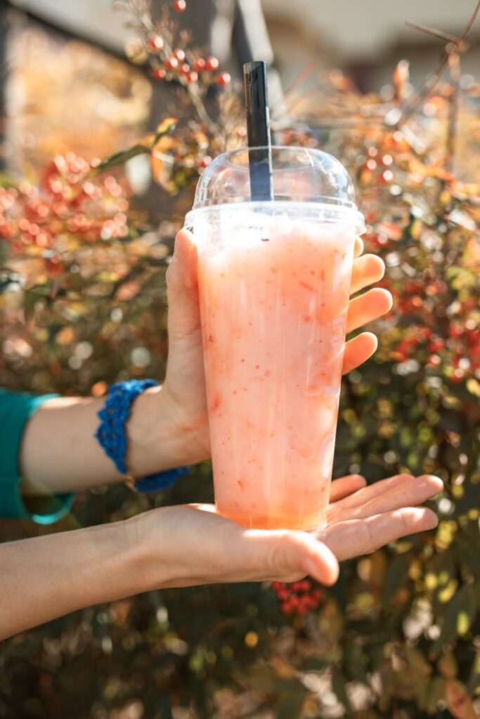 pexels-photo-6413606 Close-up of a refreshing iced strawberry drink held outdoors against a leafy background.